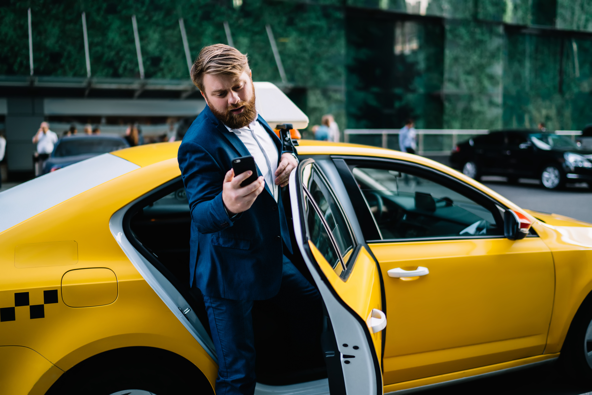 Experienced male economist sitting at yellow cab and getting to business meeting with corporate boss of enterprise doing online money transfer via banking application on modern cellular gadget